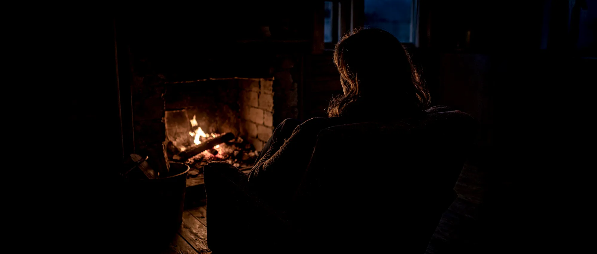 Kvinna sittande vid utdöende brasa sedd bakifrån